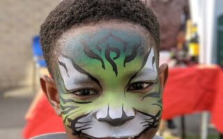 A child's face painted as a green tiger