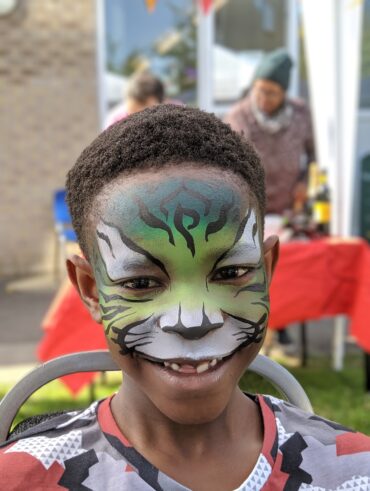 A child's face painted as a green tiger